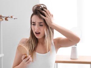 Corte Químico no cabelo. Foto mostra mulher loira olhando para a escova de cabelo assustada